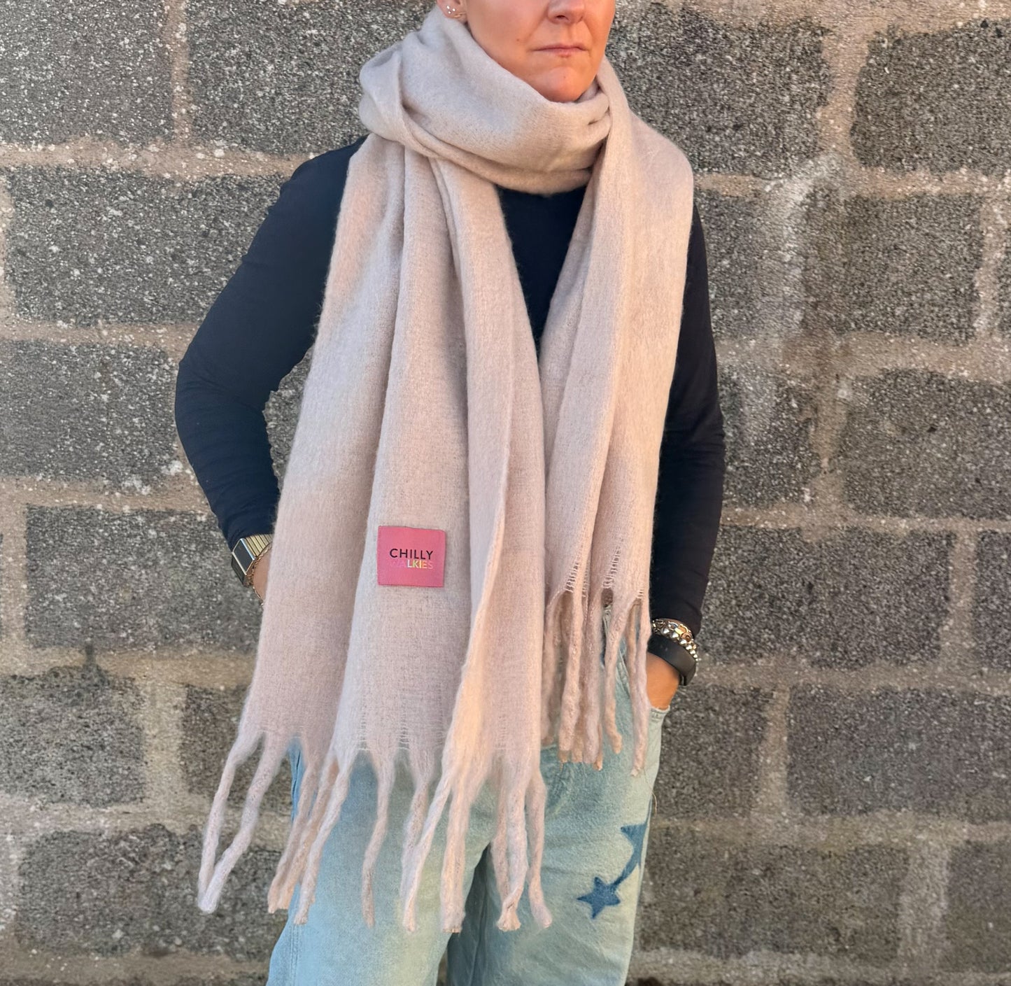 A person wearing an oversized light pink Chilly WALKIES scarf styled loosely over a black top and jeans, showing the soft drape and tasselled ends.